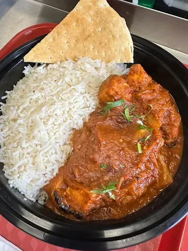 Bowl of Indian food: white rice, chicken curry, and a triangular piece of flatbread. The food is in a black bowl on a red tray.