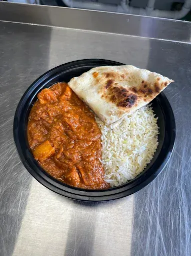 A bowl of Indian food with curry, rice, and naan bread on a metal surface.