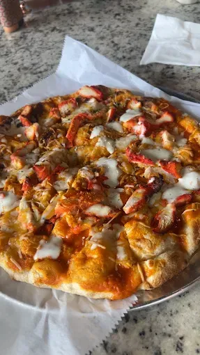 Pizza on a silver plate and white paper. It has orange chicken and white sauce, set on a table.