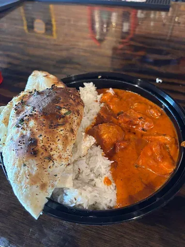 Butter chicken with white rice and naan bread in a black bowl, on a wooden table.