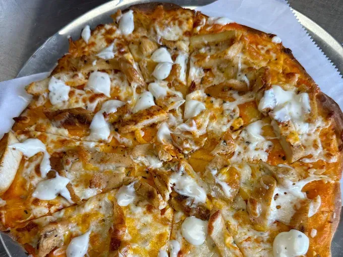 Buffalo chicken pizza, sliced, with white drizzle on a metal tray.