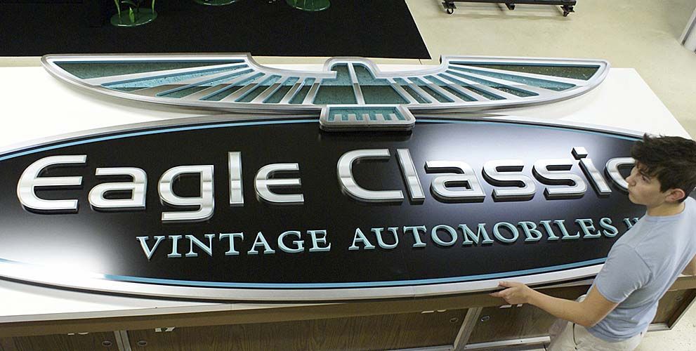 A man is working on a large sign for eagle classic vintage automobiles