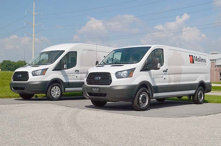 Two white vans are parked next to each other on the side of the road.