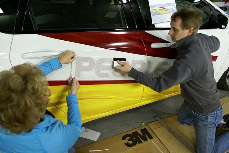 A man and a woman are wrapping a car in yellow and red