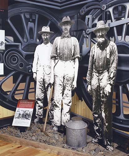Three men are standing in front of a large wheel