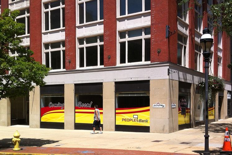 A man walking in front of a building that says people 's bank