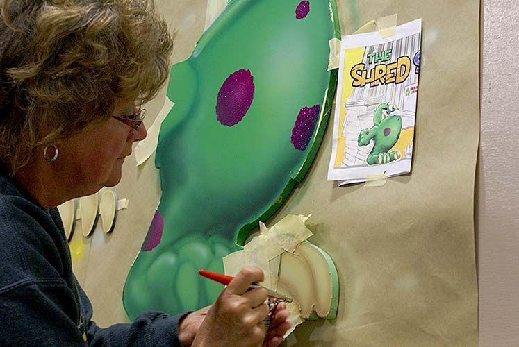 A woman is painting a picture of a dinosaur on a wall.
