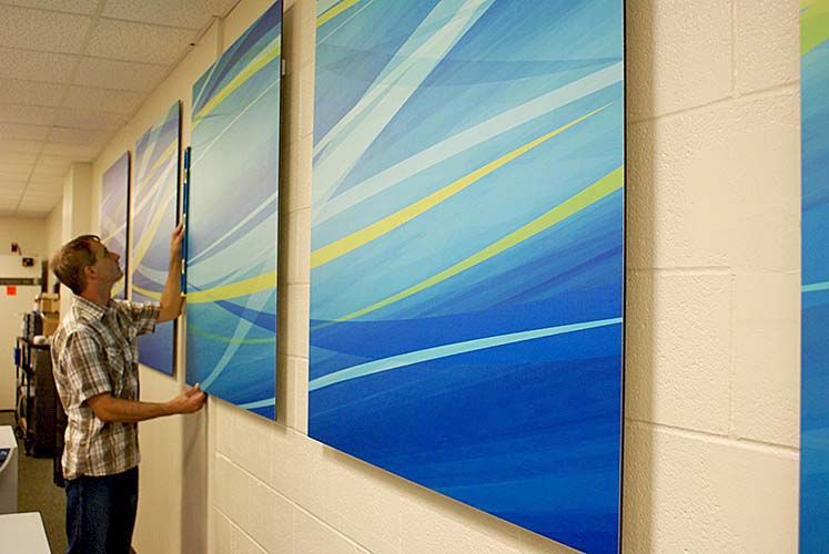 A man is hanging a blue and yellow painting on a wall