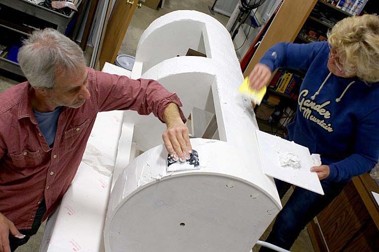 A man and a woman are working on a large white object.