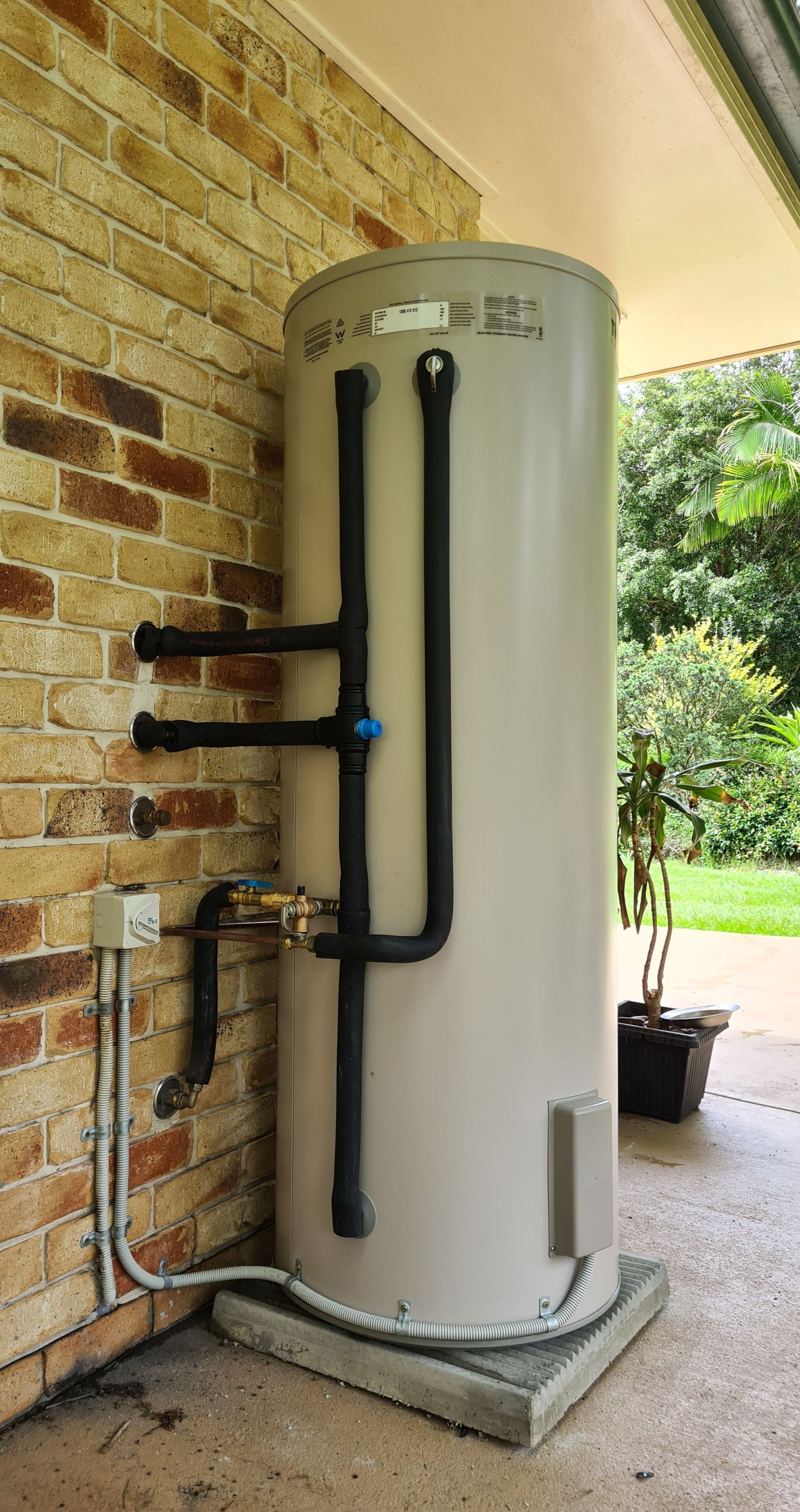 A Man Is Sitting on The Grass Fixing an Air Conditioner — 24/7 HOT H2O in Valdora, QLD