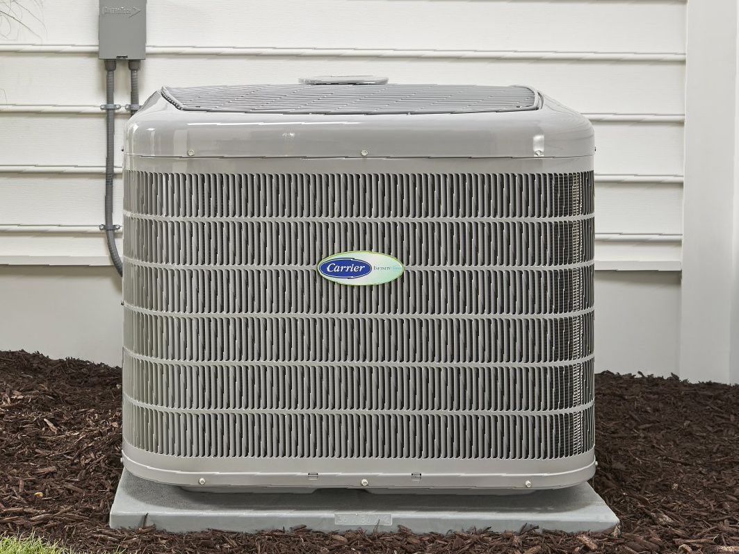 A carrier air conditioner is sitting outside of a house.