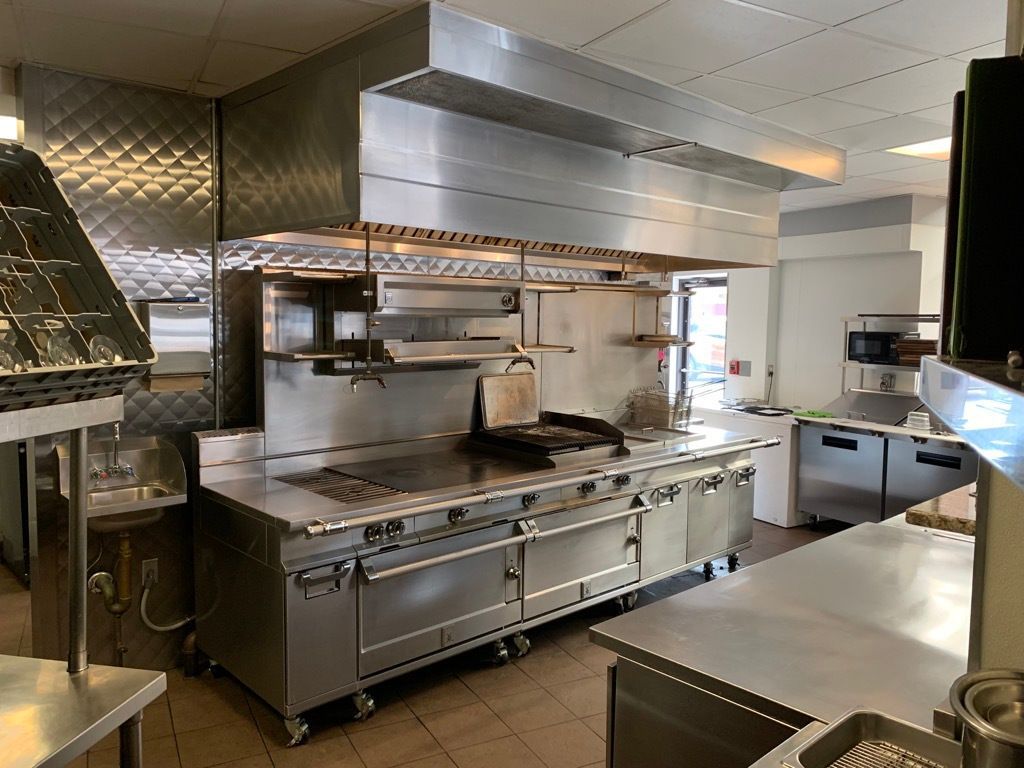 A large commercial kitchen with a lot of stainless steel appliances.