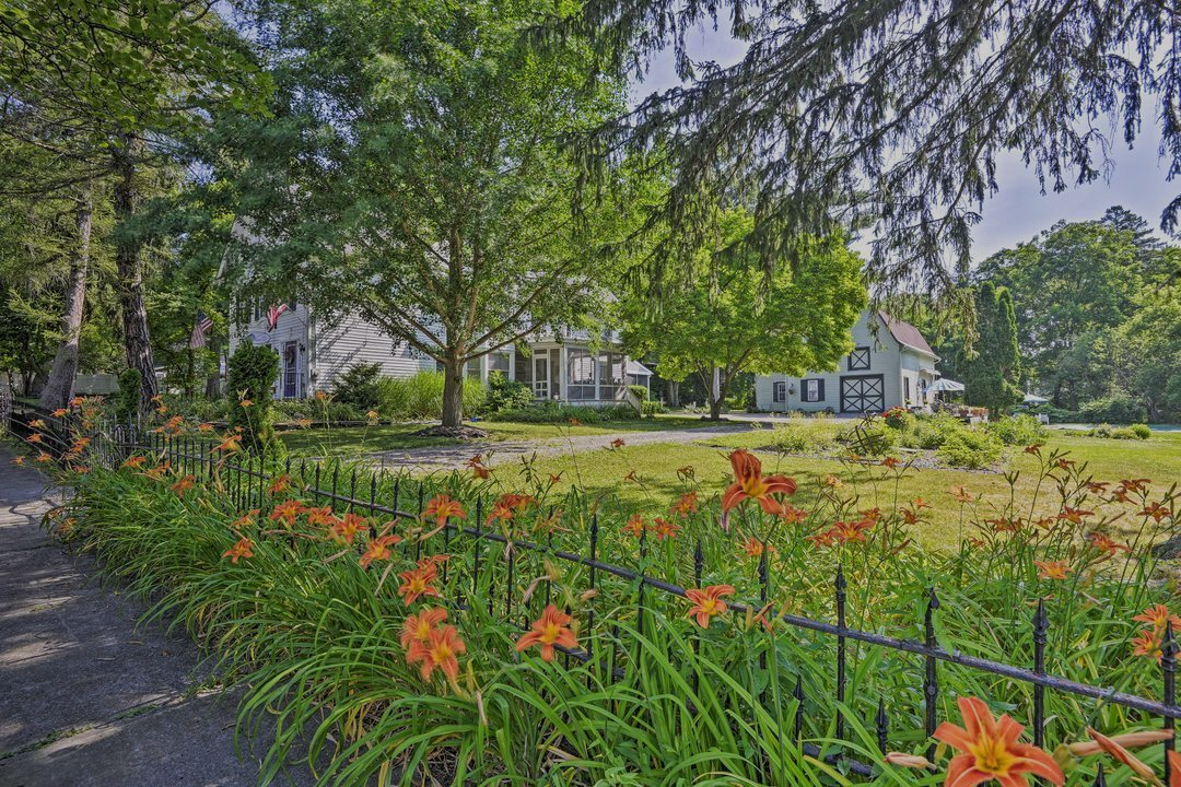 A fire pit surrounded by red chairs on a grassy hill, with a house and trees in the background.