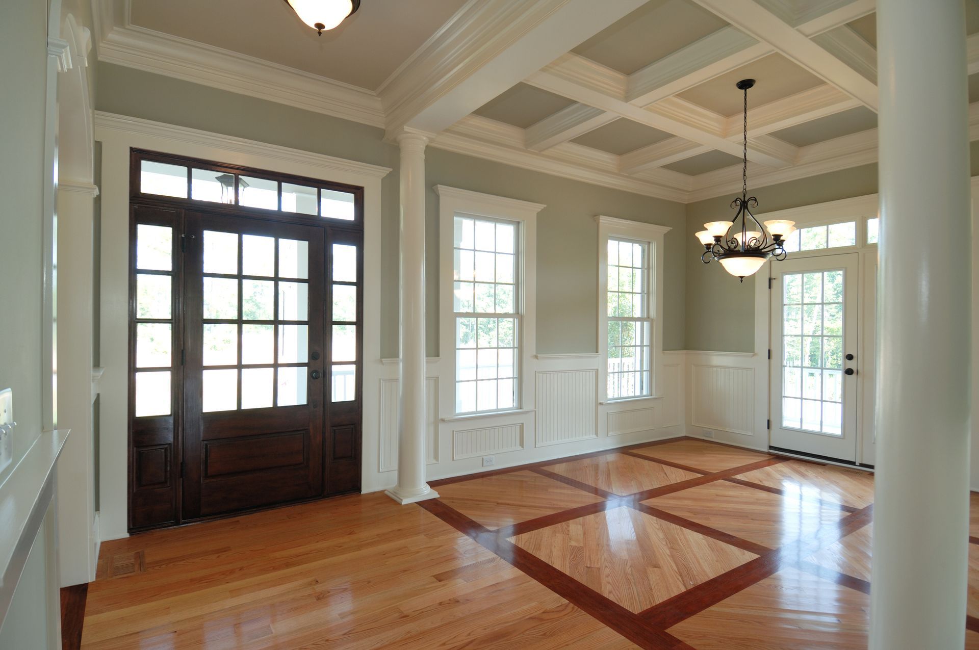 Elegant entryway with wood floors, detailed trim, glass door, and chandelier.