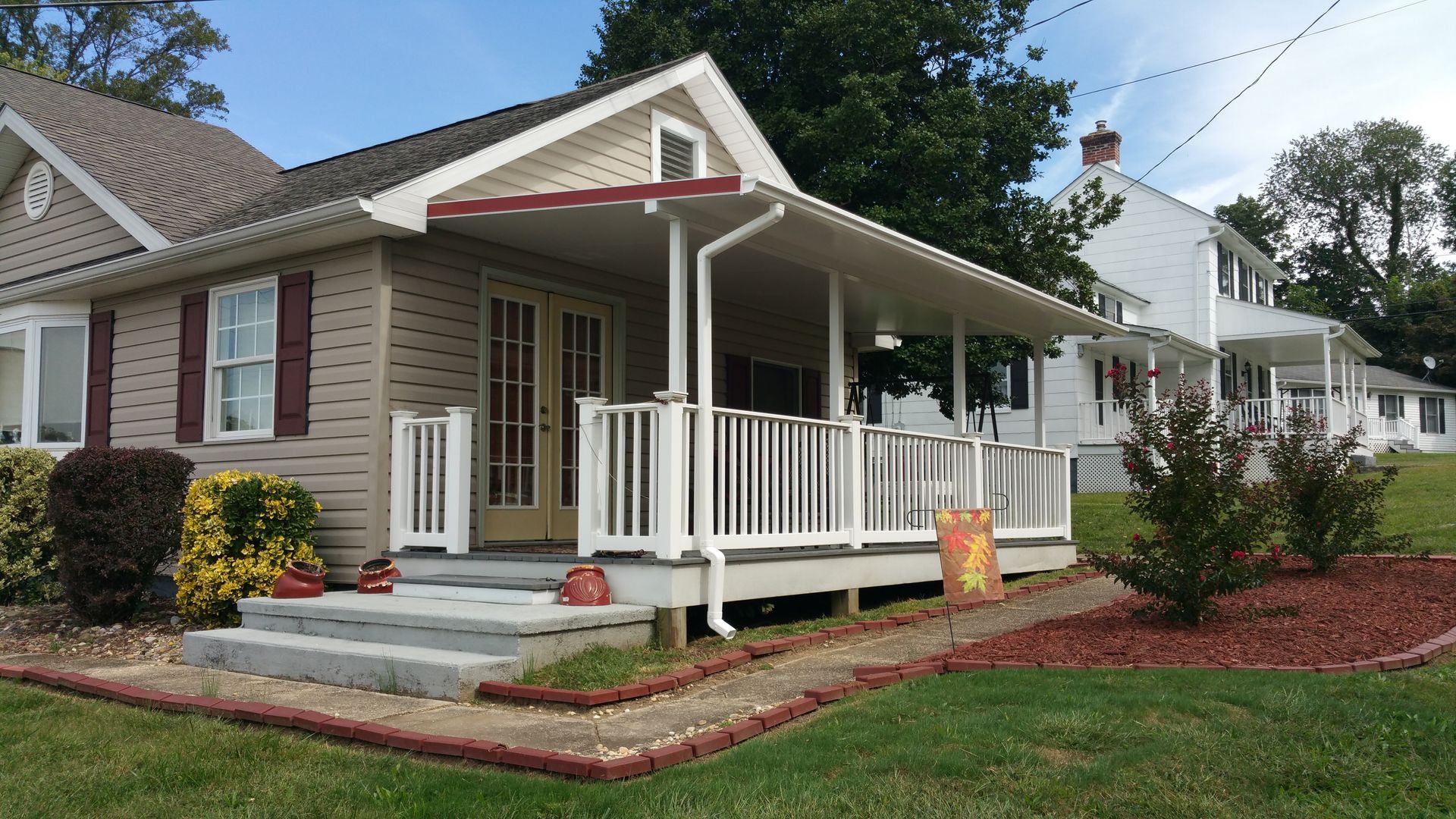 Tan house with covered porch and white railing, steps leading to the entrance, front yard.