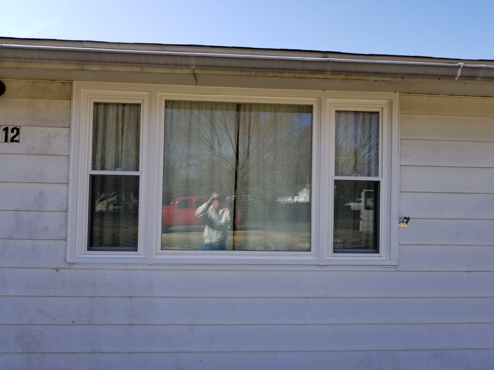 Window with white frame on a white house. Trees and red vehicle reflected in window.