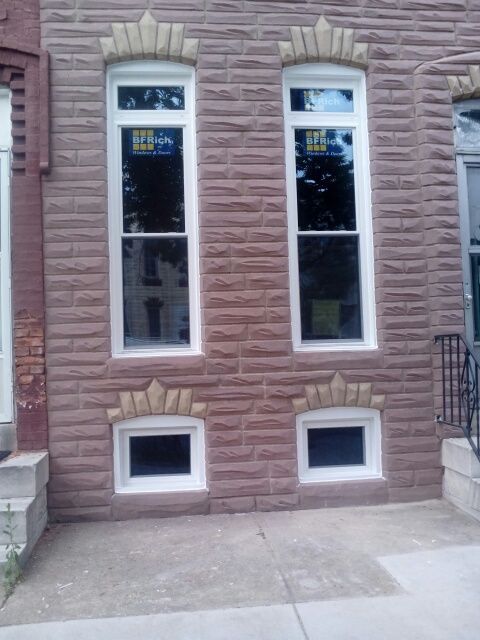 Two tall, rectangular windows and two small square windows in a brick building with decorative stone accents.