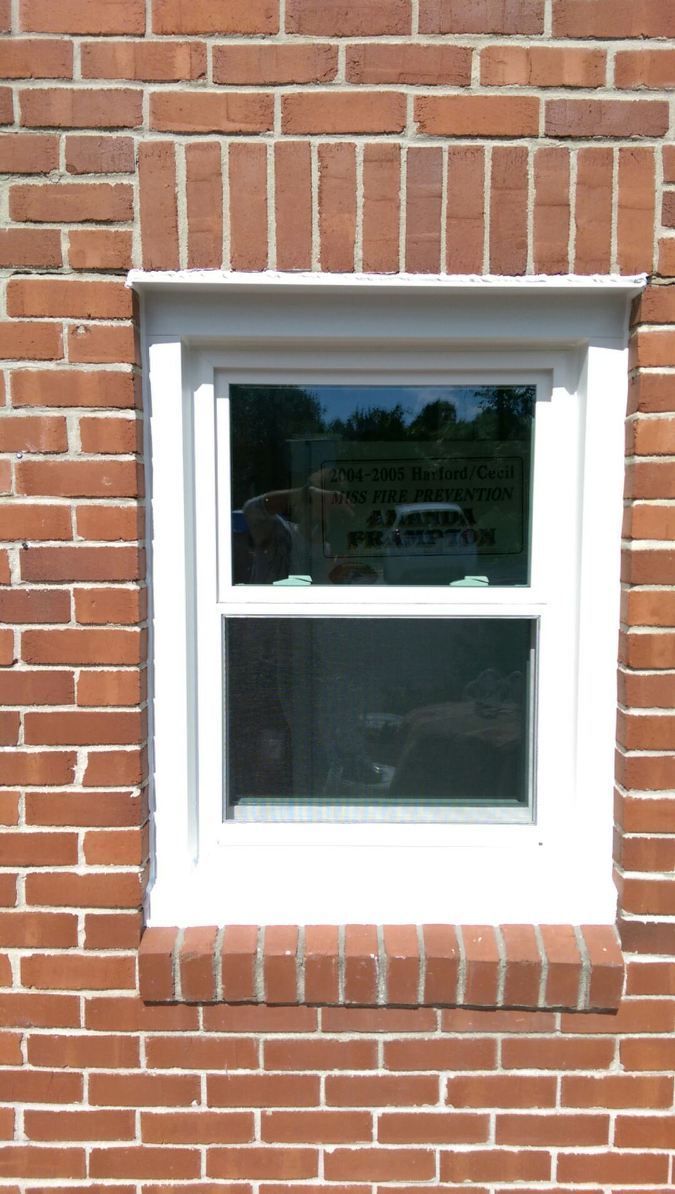 White-framed window in a red brick wall, reflecting trees and sky.