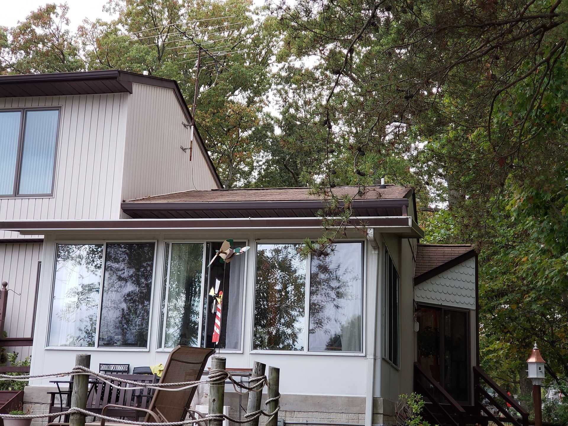 House with porch, glass windows, wooden siding, and surrounded by trees.