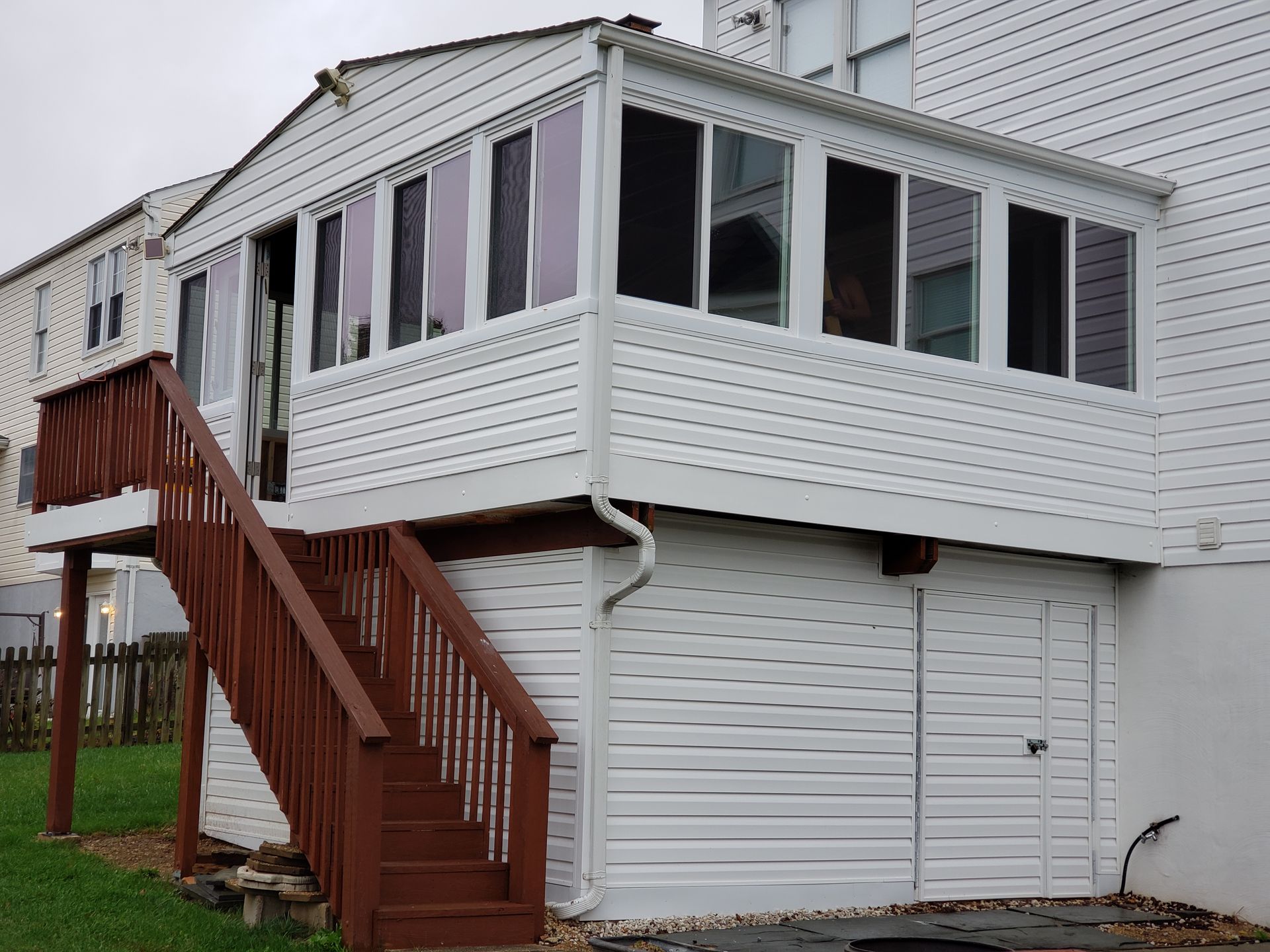 Back of a two-story house with a screened porch and wooden stairs leading to a deck; white siding.