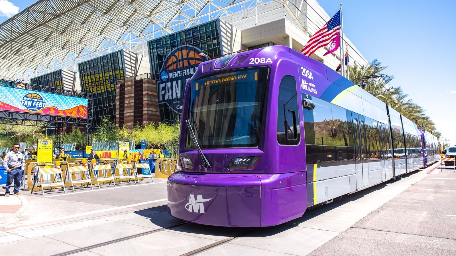 Modern bus stop with people waiting, trees, and a building with glass windows on a sunny day.