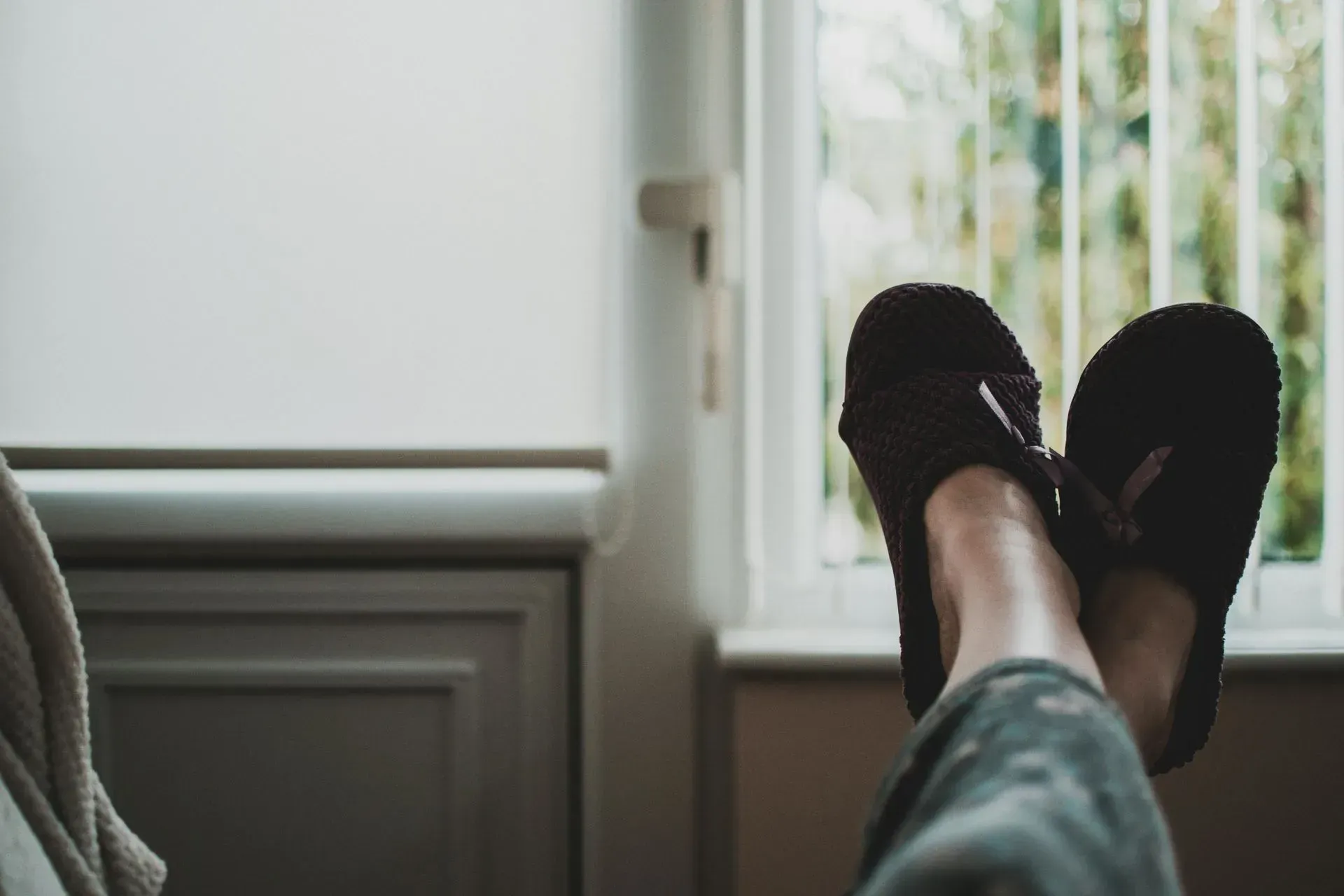 A person wearing slippers is sitting in front of a window.
