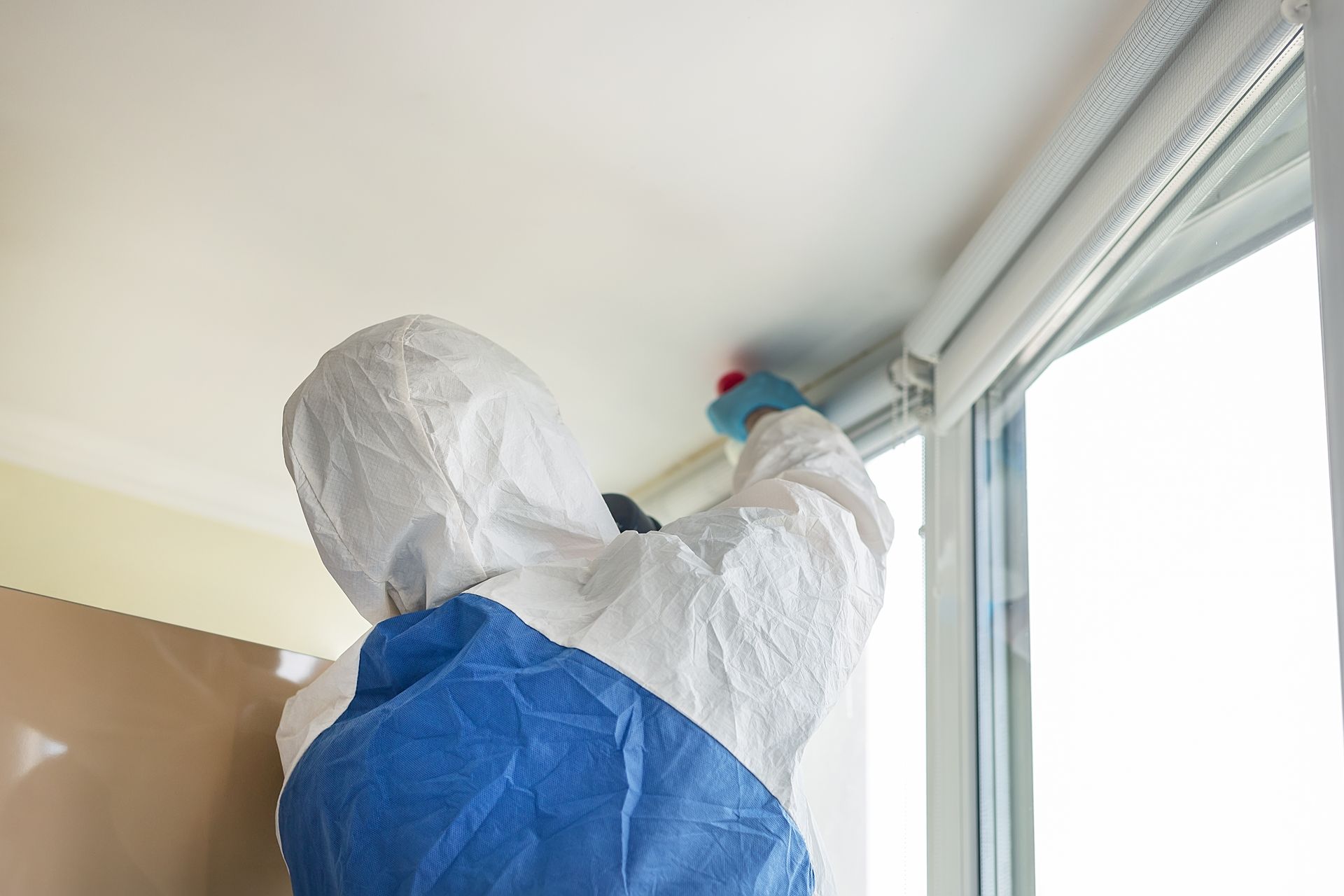 A person in a protective suit is cleaning the ceiling of a room.