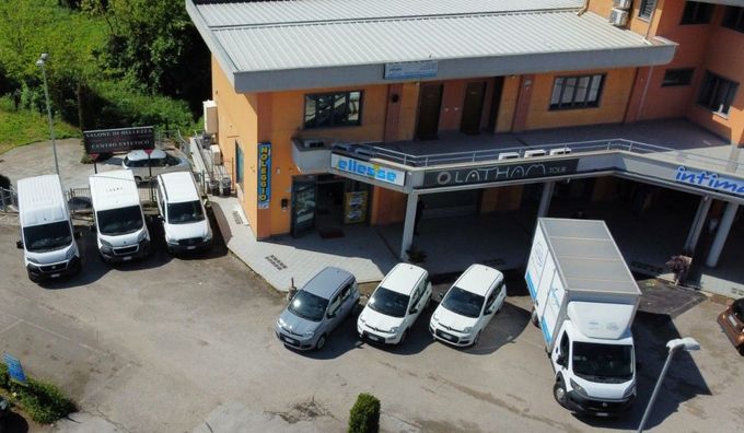 Diversi camion e furgoni bianchi erano parcheggiati davanti a un edificio arancione con un ingresso coperto.