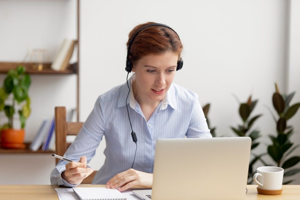 A Woman Wearing Headphones is Sitting at a Desk Using a Laptop — Repo Busters Wyong In Wyong, NSW