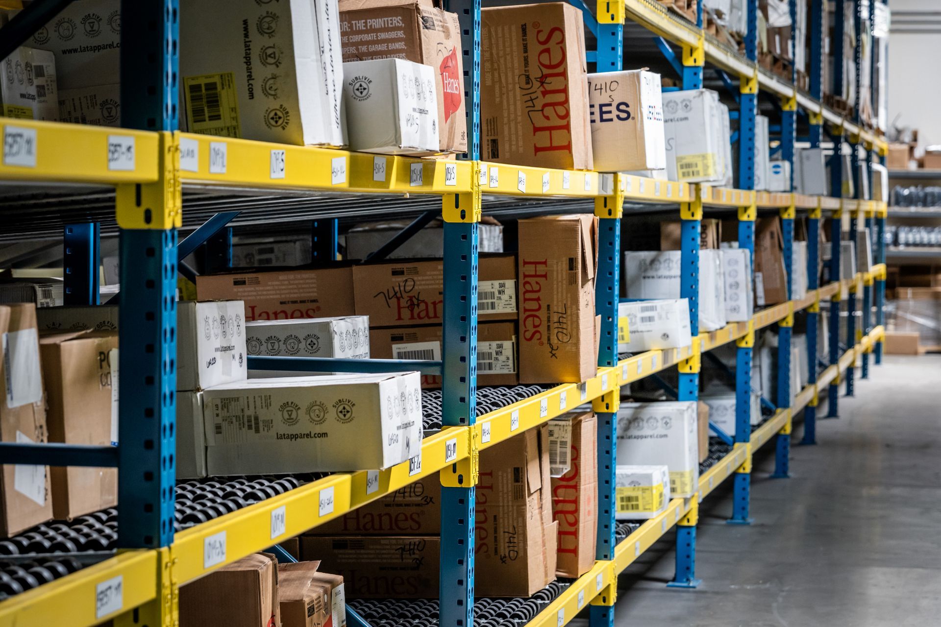Warehouse shelves filled with cardboard boxes. Yellow and blue metal structure in a brightly lit space.