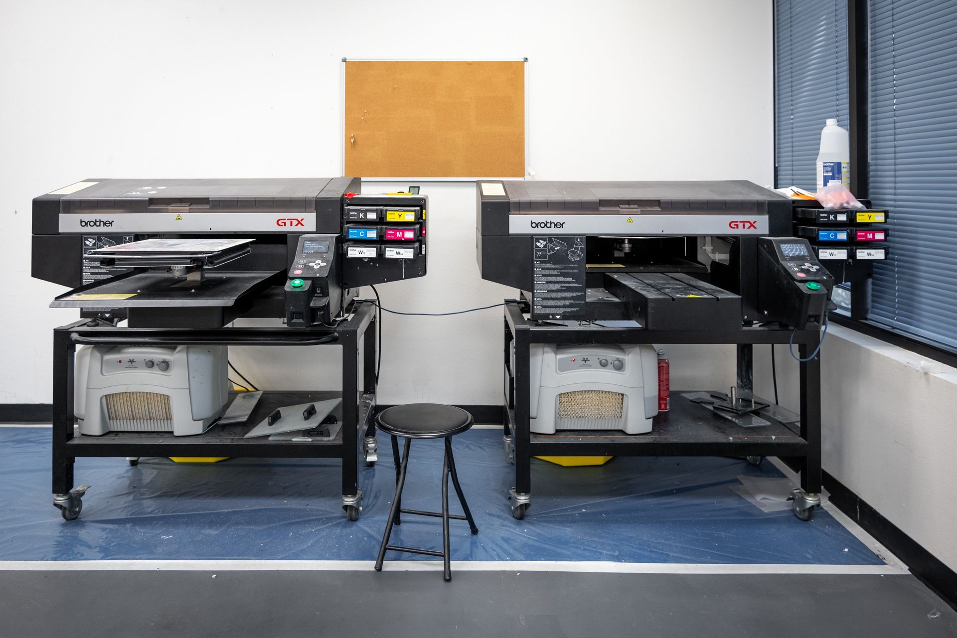 Two large industrial printers on rolling carts, with a small stool in front of them, in a printing workshop.
