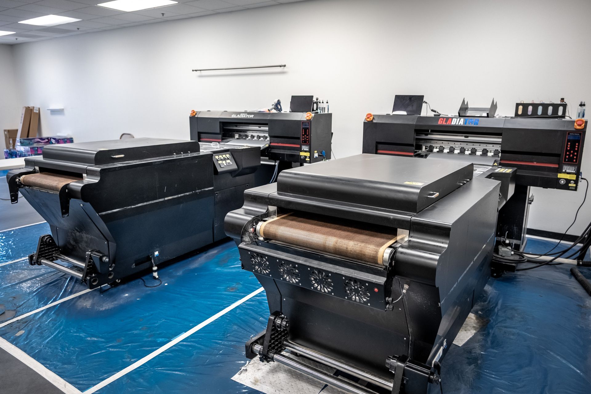 Three large industrial printers in a room with blue flooring.