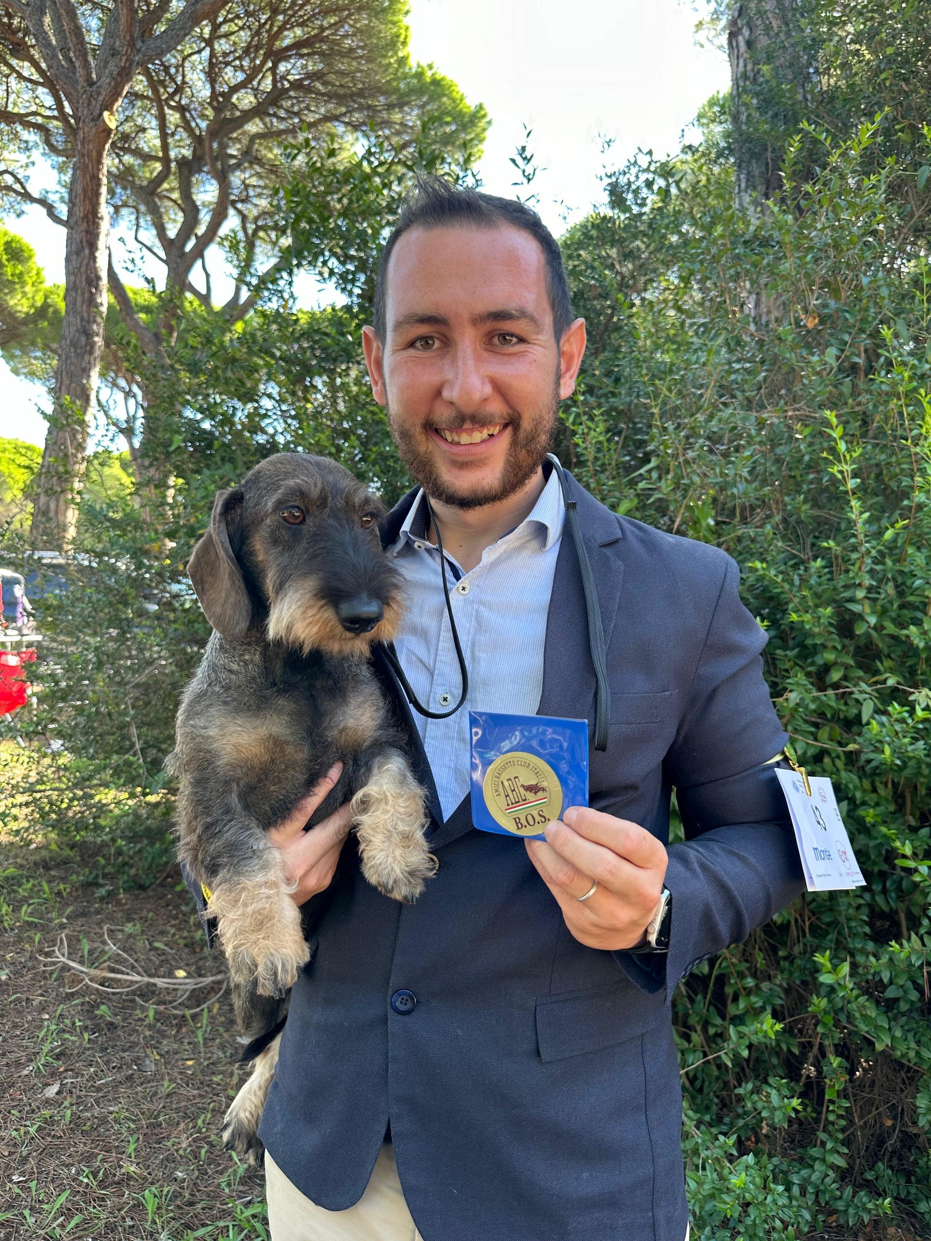 Un uomo tiene in braccio un cagnolino e una medaglia.