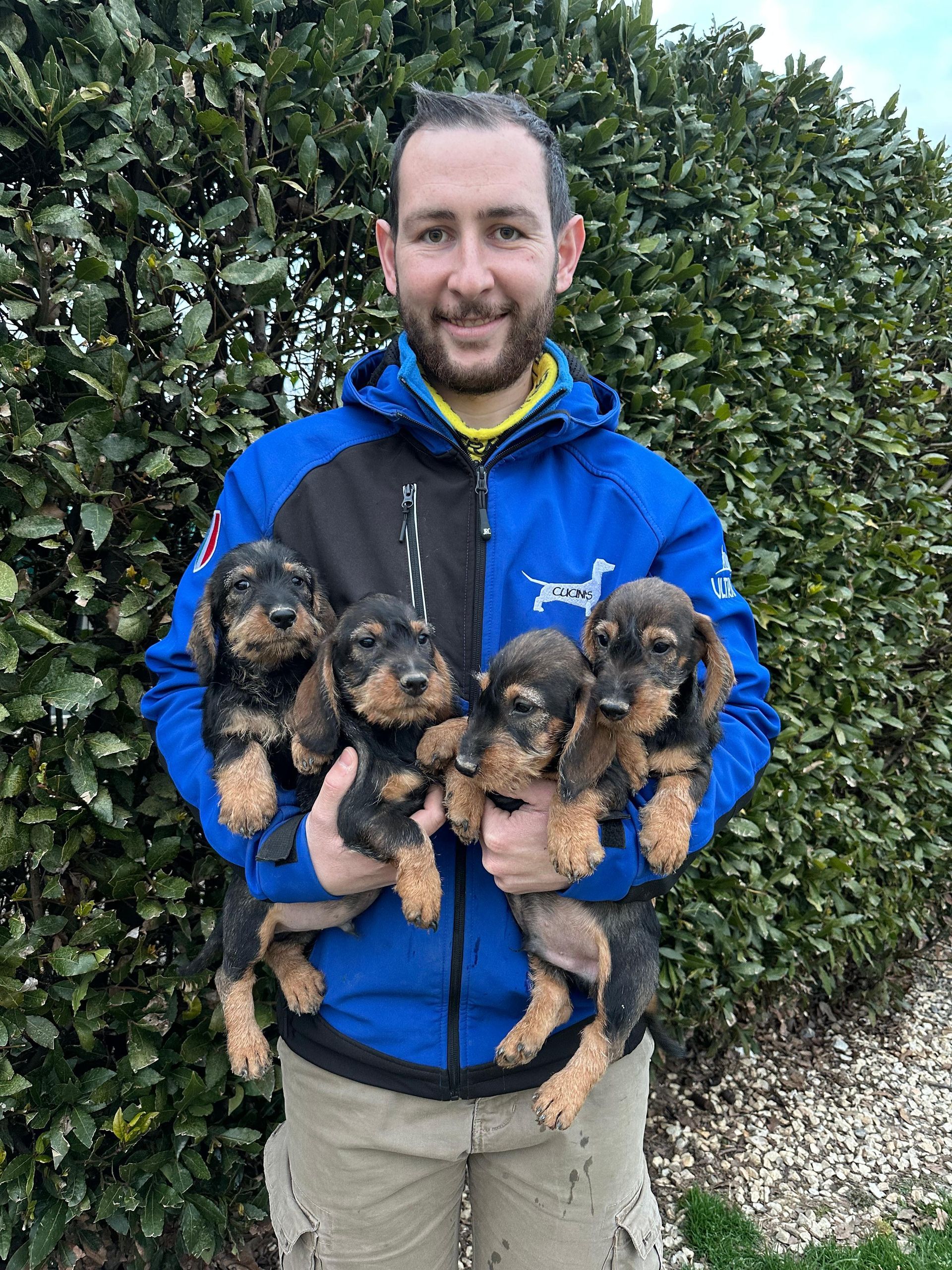 Un uomo con una giacca blu tiene tra le mani quattro cuccioli.