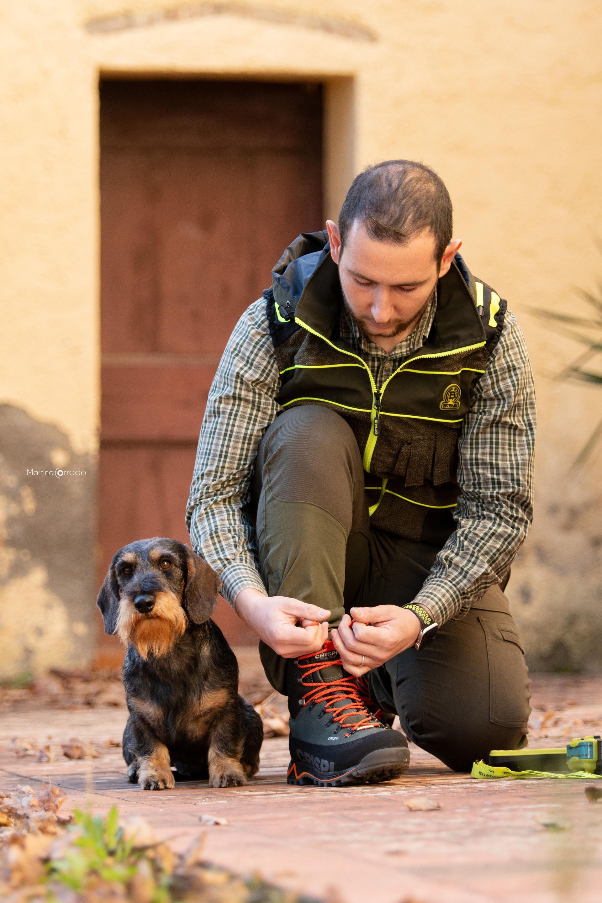 Un uomo si sta allacciando le scarpe accanto a un cagnolino.