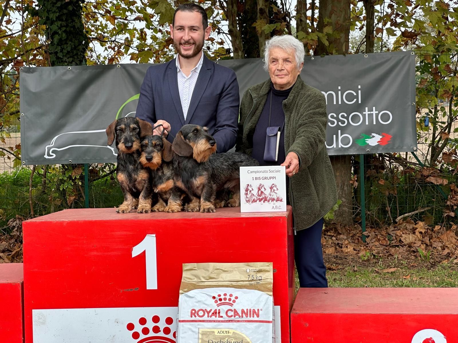 Un uomo e una donna sono in piedi su un podio con tre cuccioli di bassotto.