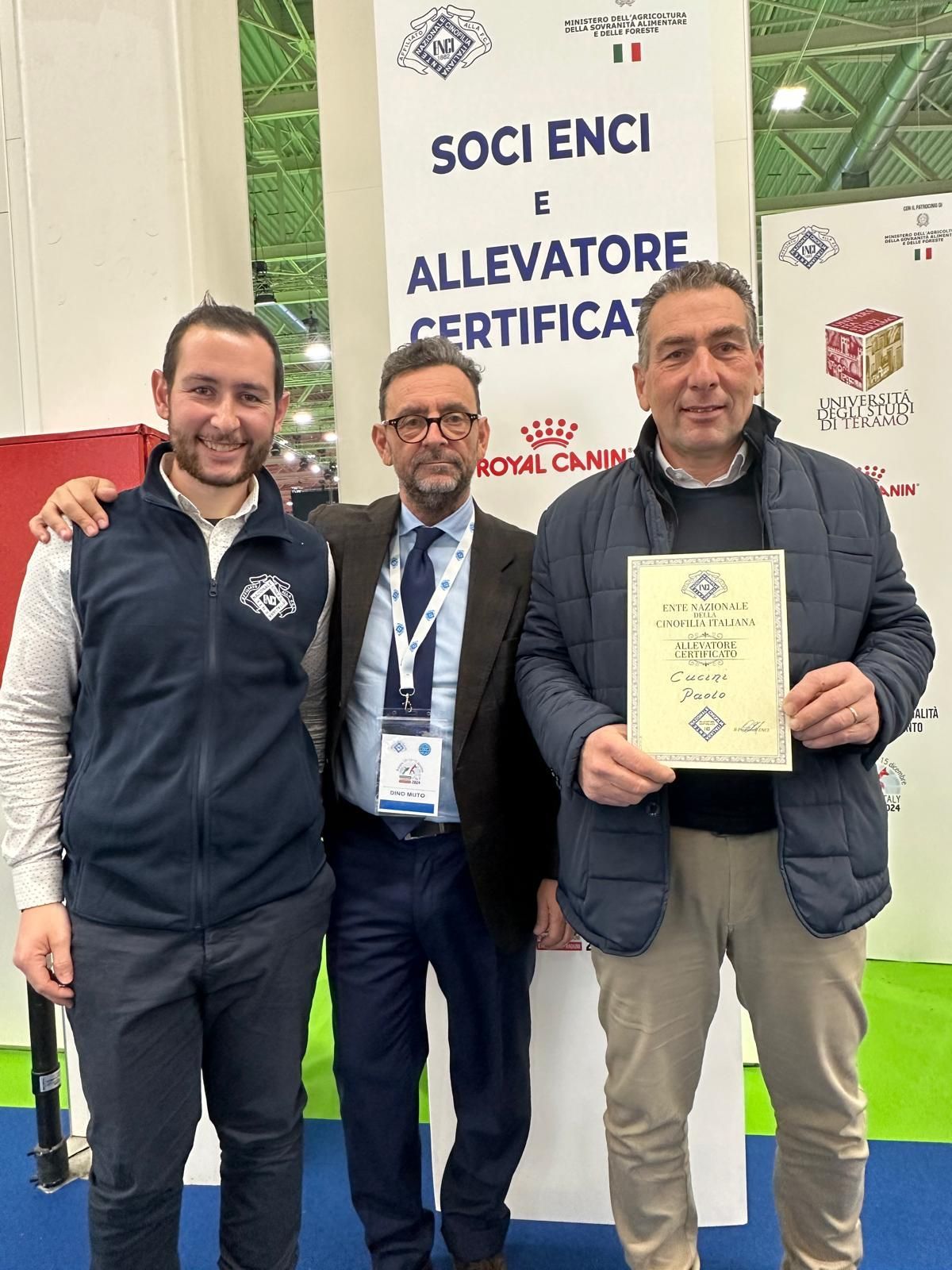 Tre uomini posano per una foto davanti a un cartello.