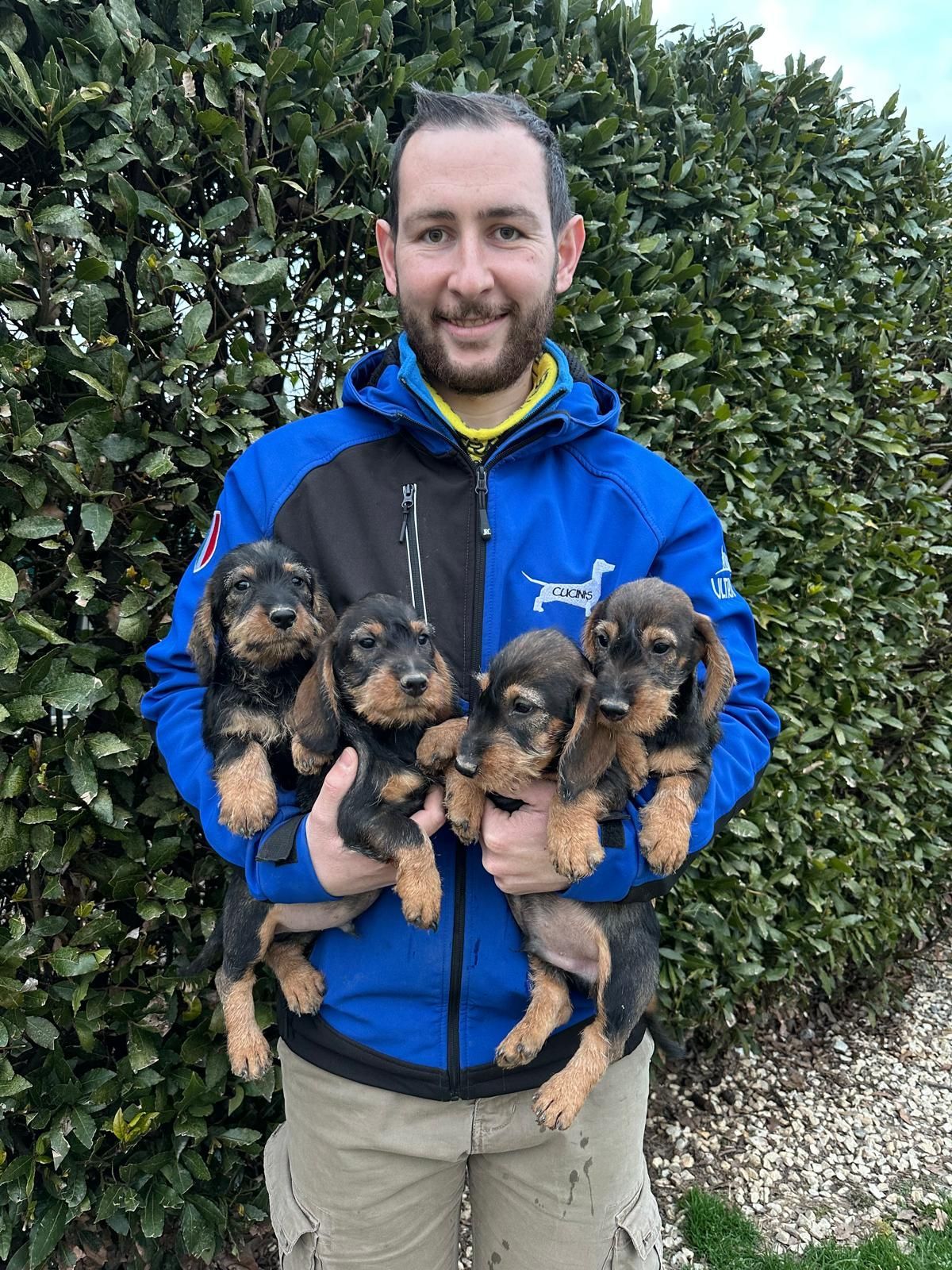 Un uomo con una giacca blu tiene tra le mani quattro cuccioli.