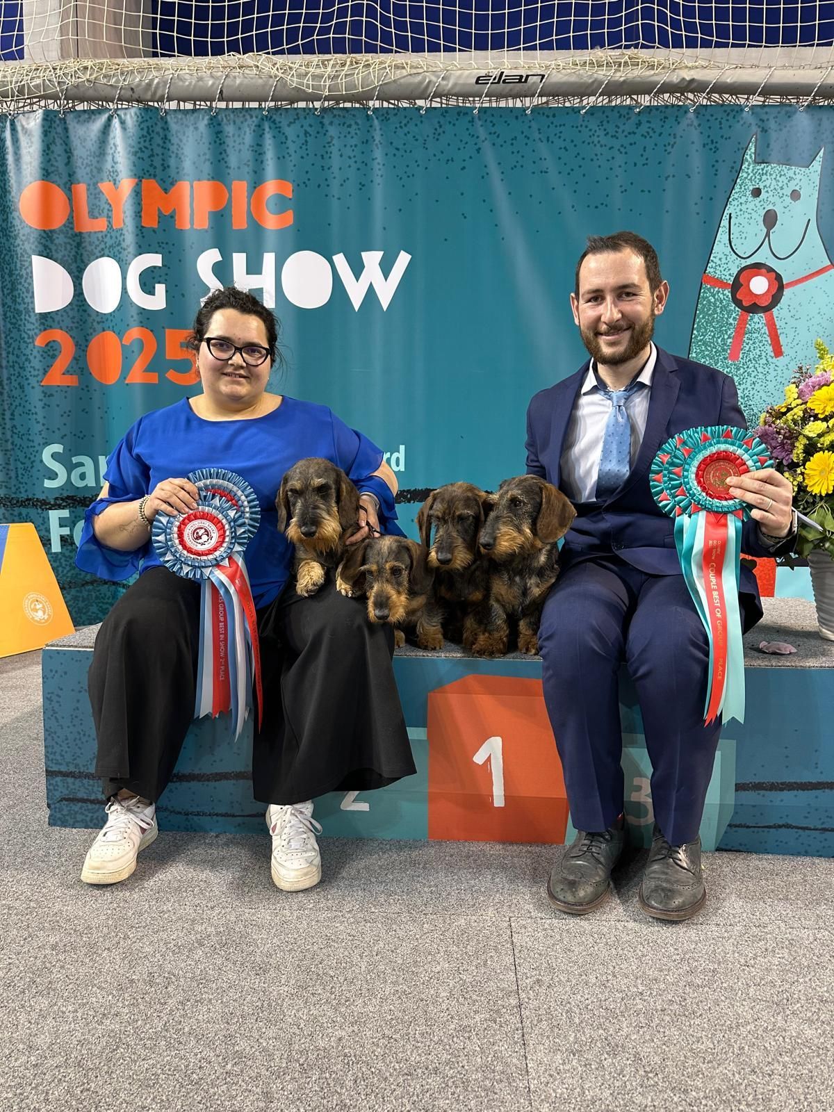 Un uomo e una donna posano per una foto con i loro cani alla mostra canina olimpica.