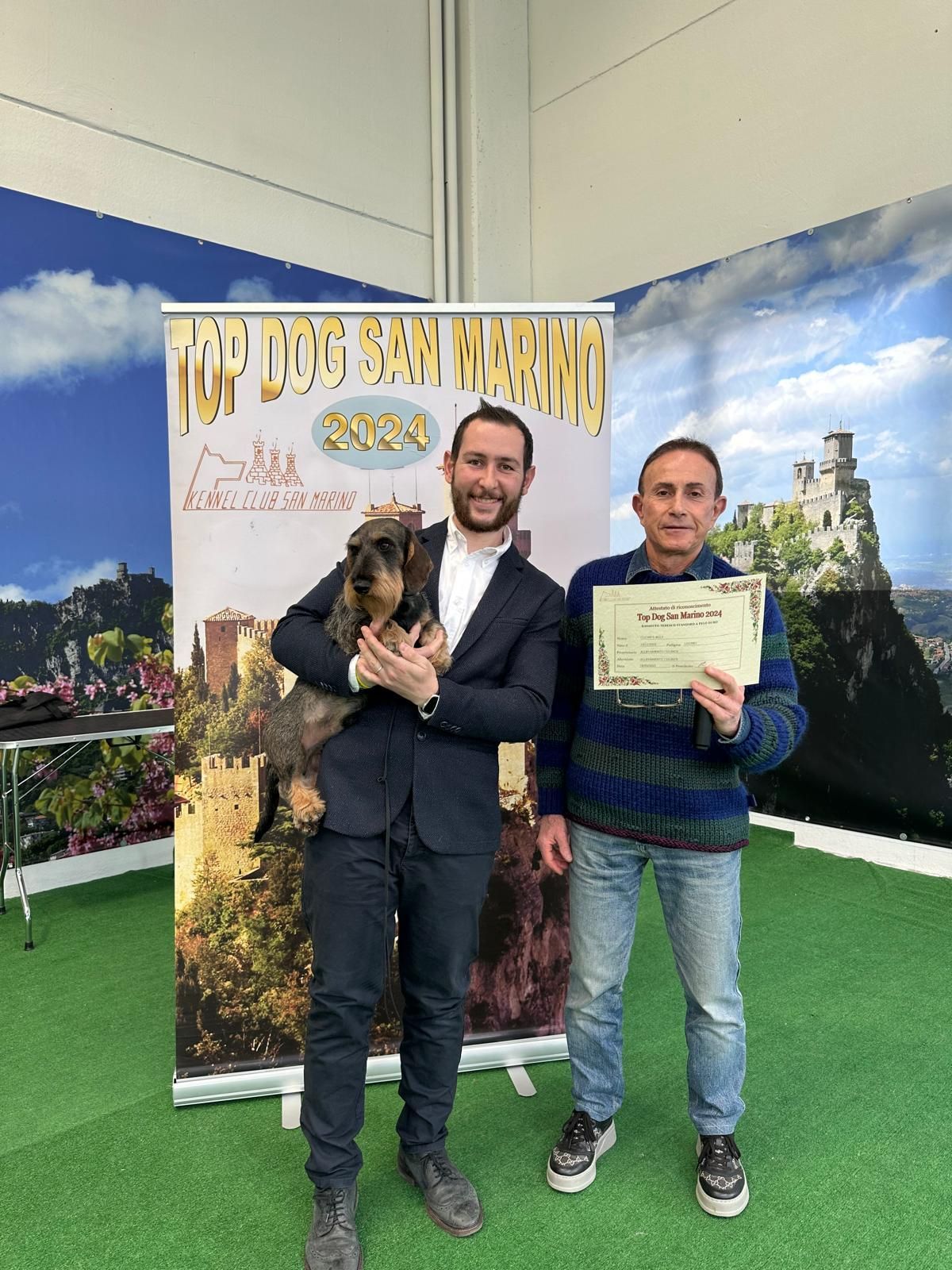 Due uomini sono in piedi uno accanto all'altro e tengono in mano un cane e un certificato.