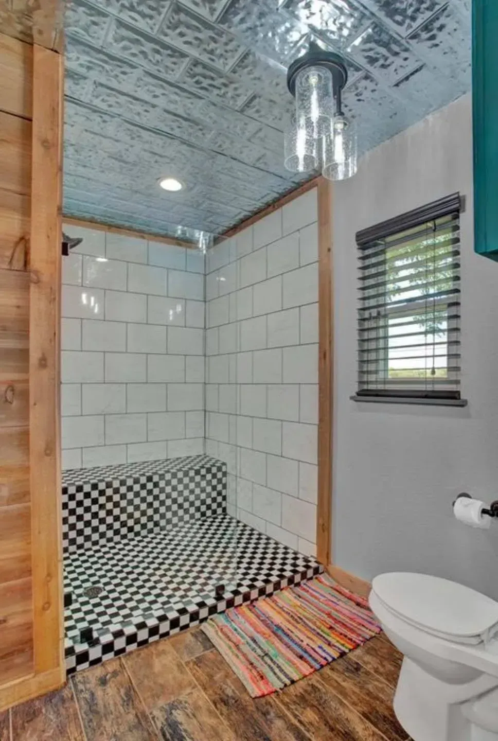 Bathroom with a black-and-white tiled shower, wood floor, gray walls, and tin ceiling.