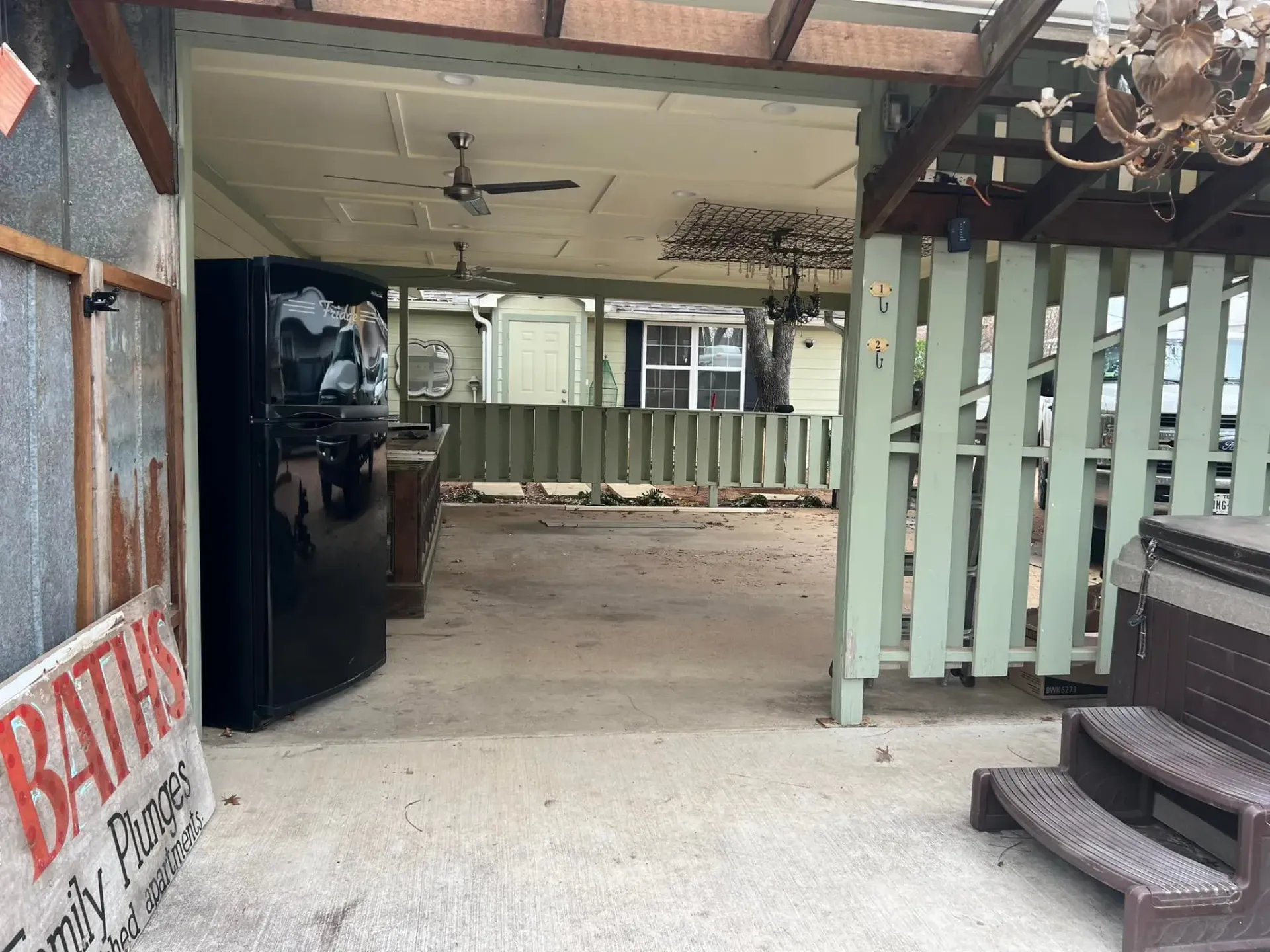 Outdoor covered area with refrigerator, fence, ceiling fan, and sign.