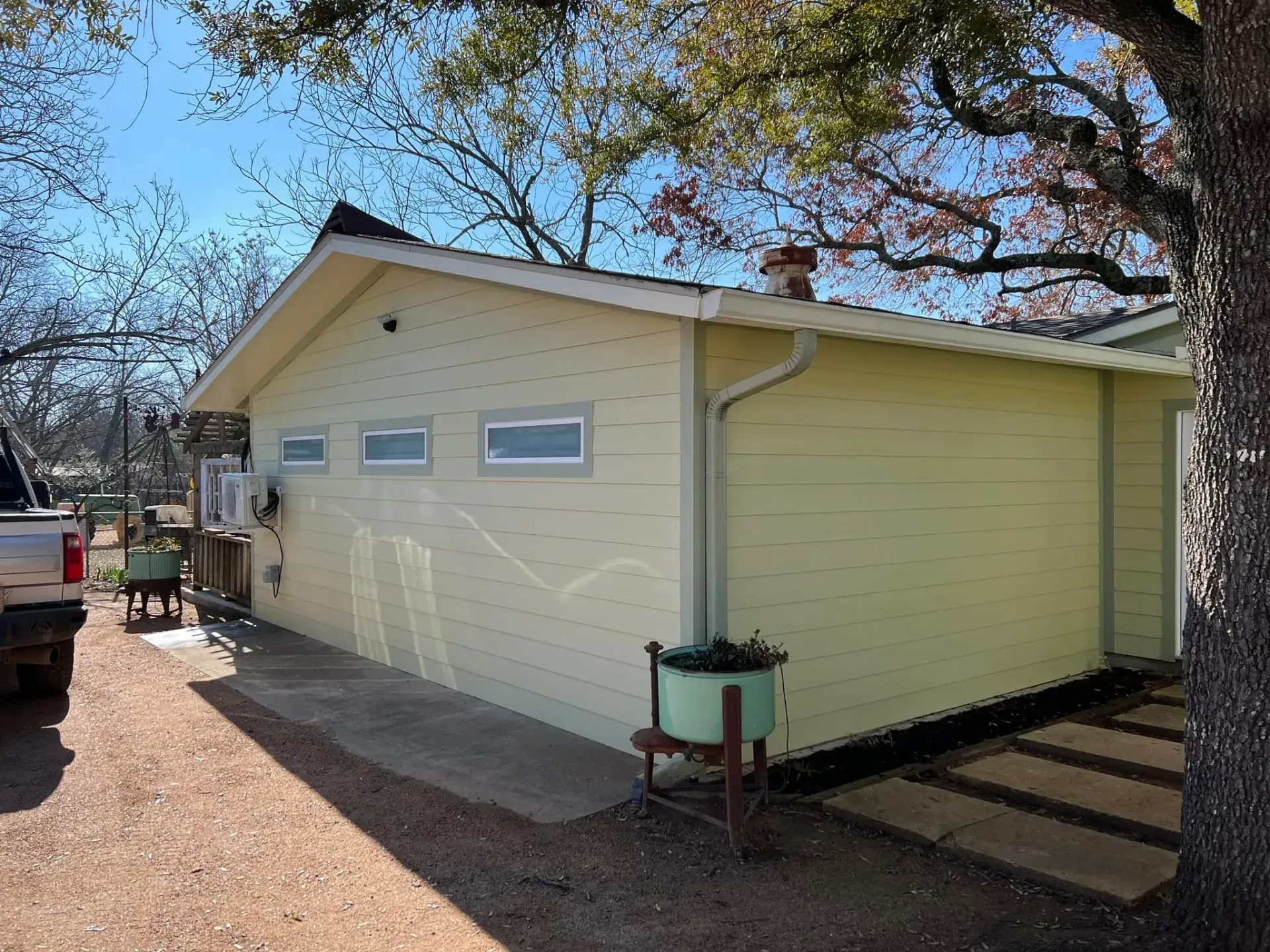 Light yellow building with small windows, chimney, and gutter under a clear, sunny sky.