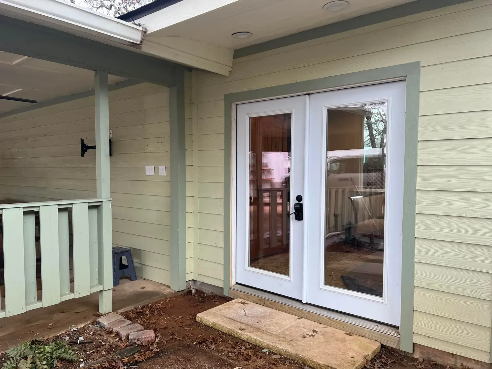 Exterior view of a light yellow house with white-framed glass double doors and light green trim.
