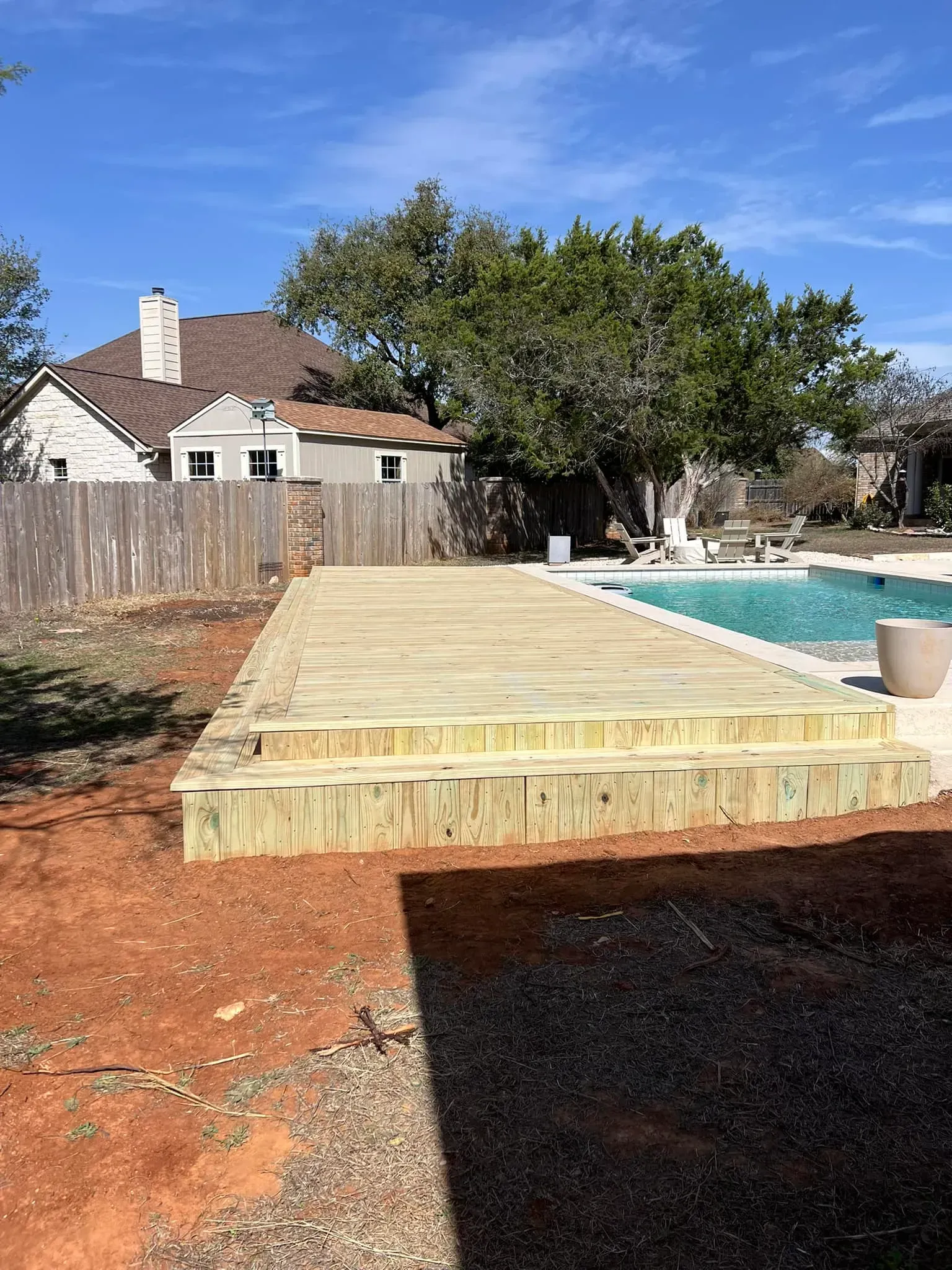 Wooden deck with steps in a backyard, beside a pool.