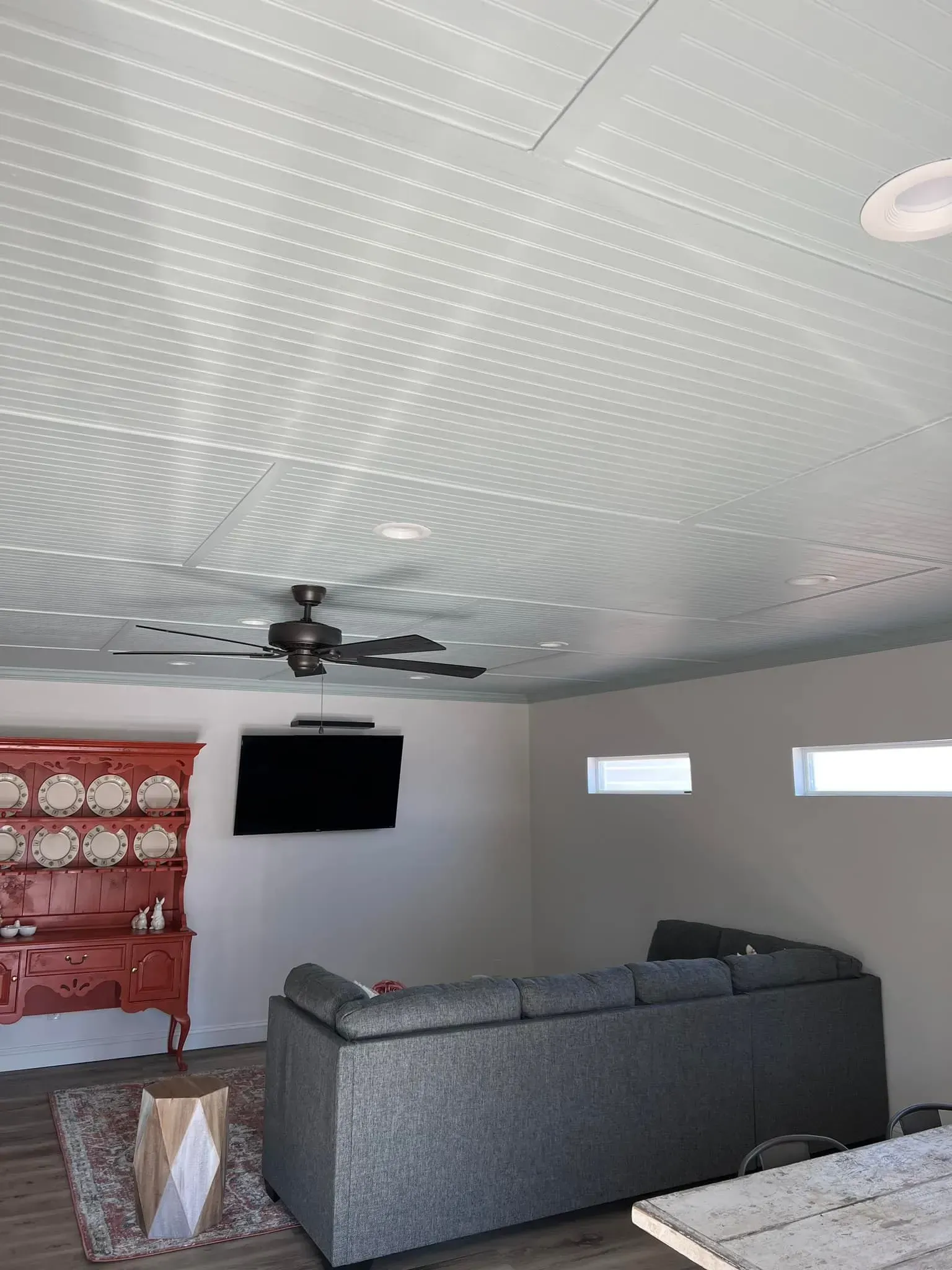 Living room with gray sofa, TV, ceiling fan, red cabinet, light green patterned ceiling.