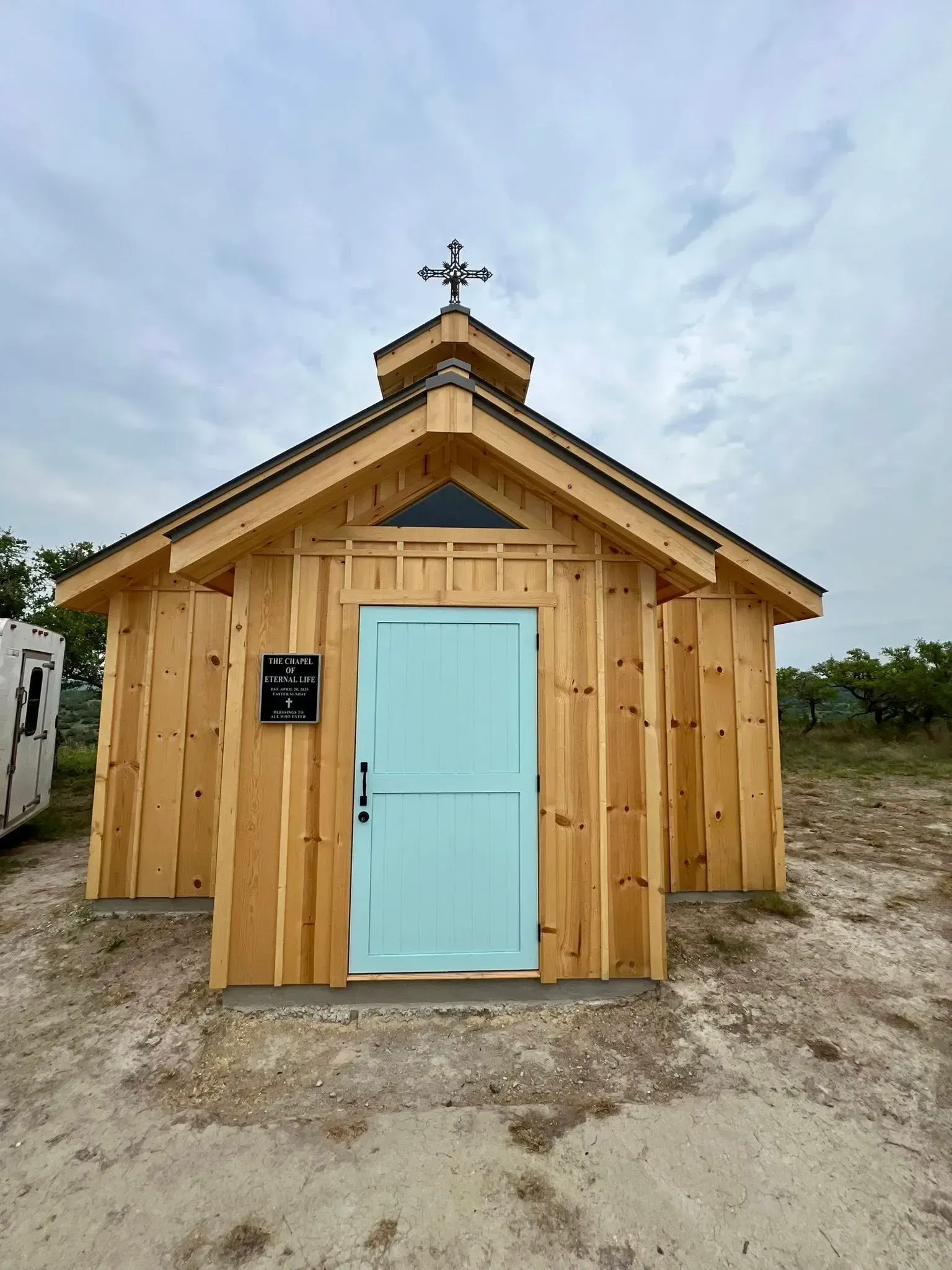 Small wooden chapel with a light blue door under a cloudy sky.