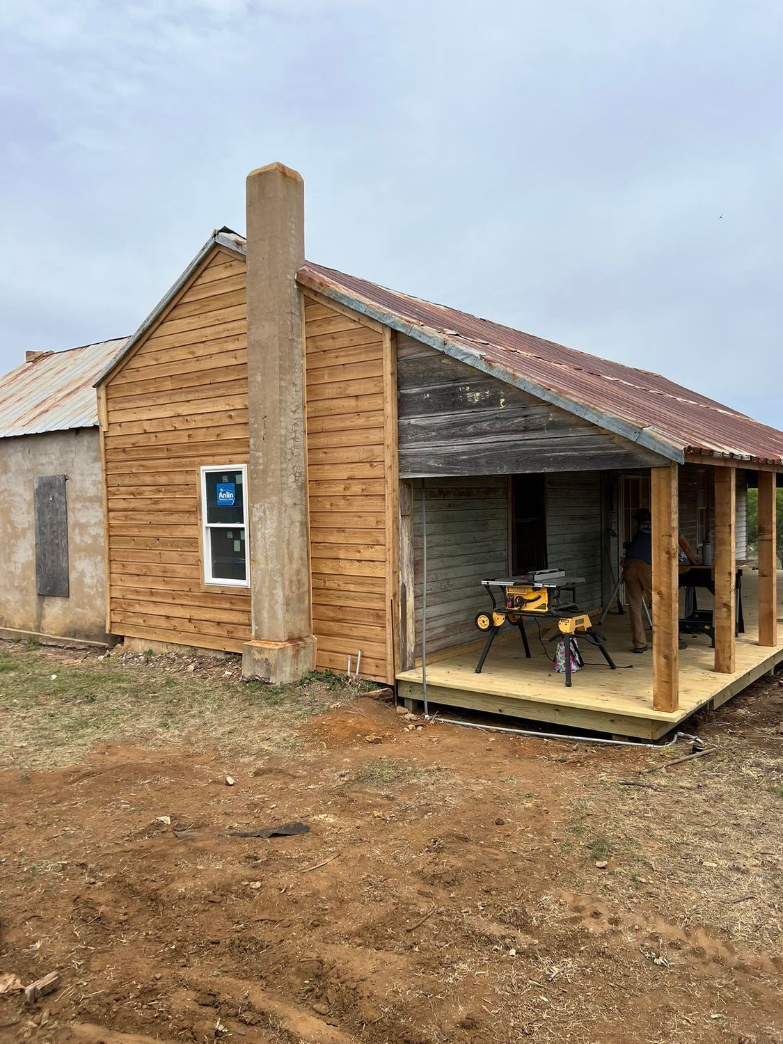 House under construction with a new porch and siding, cloudy sky in the background.