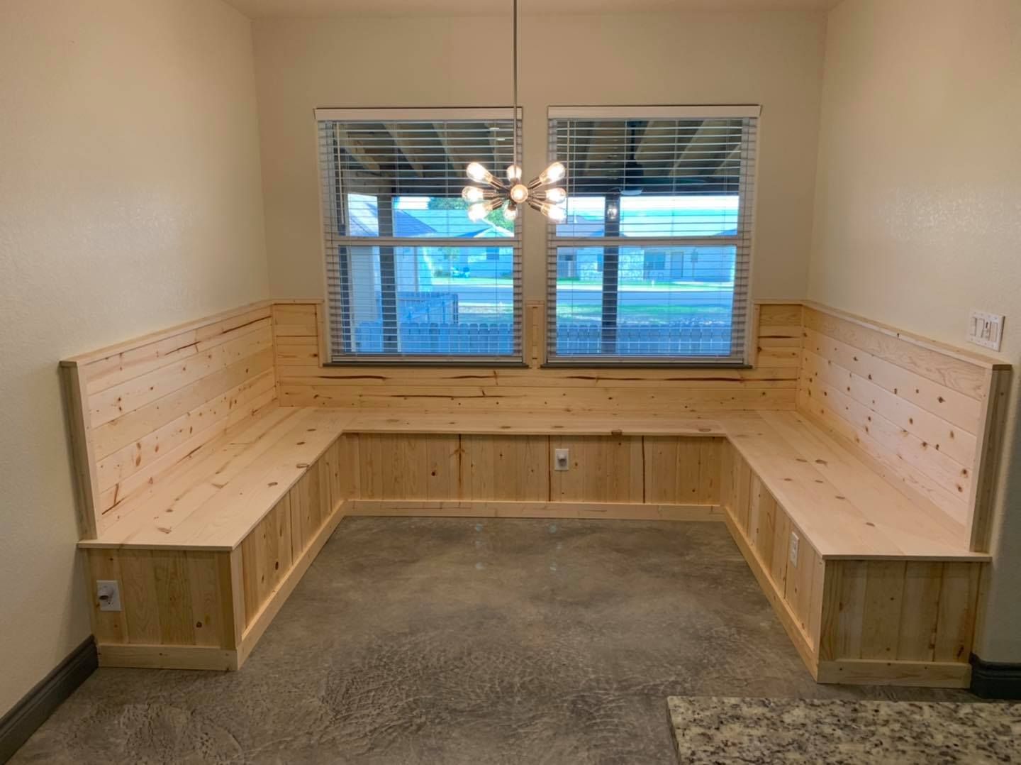 U-shaped wooden bench seat built into a dining nook with two windows. A light fixture hangs above.