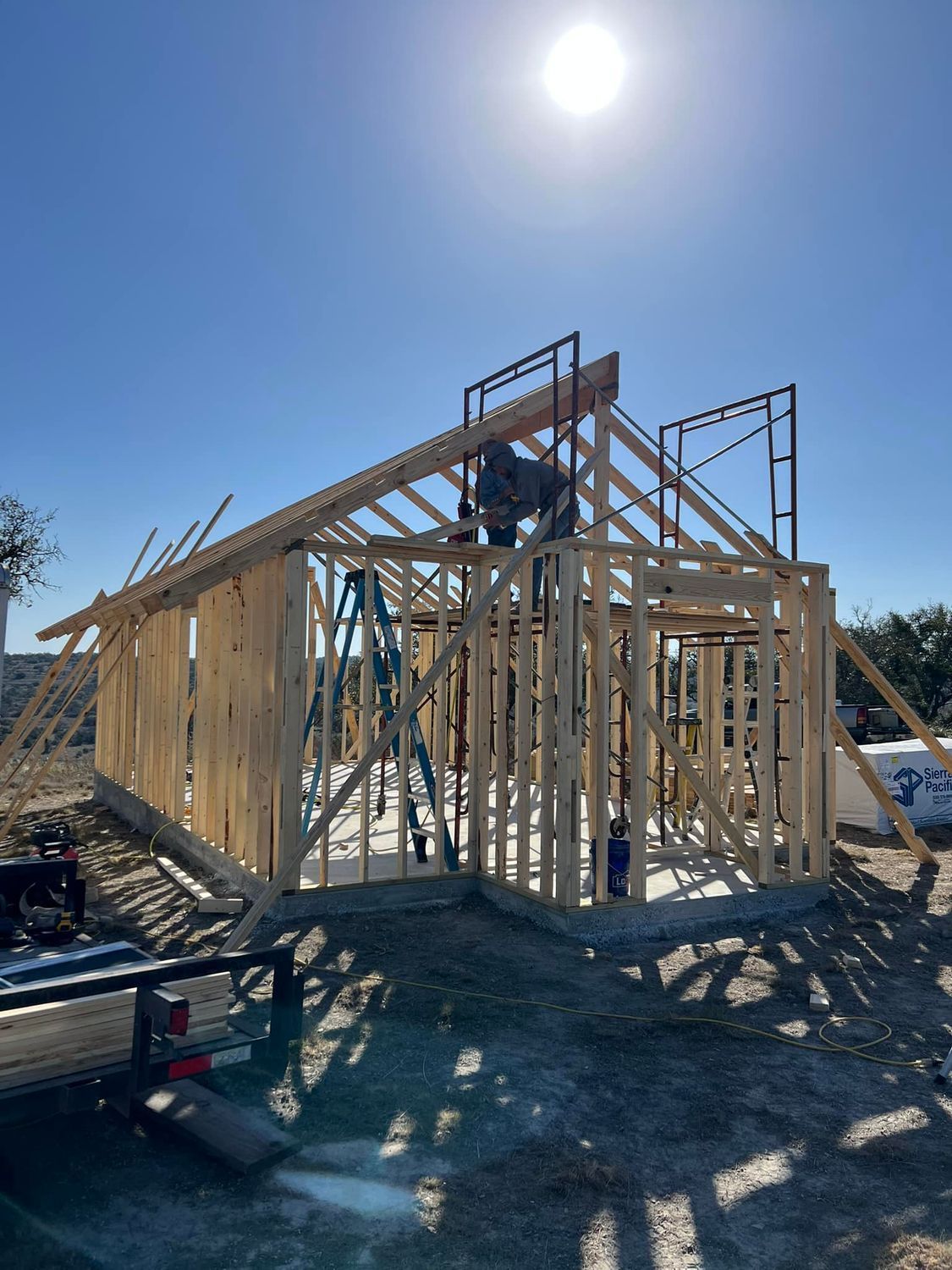 Construction of a wooden building frame under a bright sun. A worker is on scaffolding.